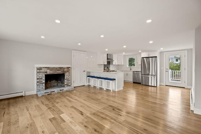 unfurnished living room featuring recessed lighting, a baseboard heating unit, a sink, and light wood-type flooring