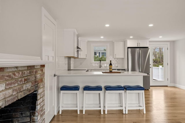 kitchen featuring white cabinets, freestanding refrigerator, a peninsula, a kitchen bar, and backsplash