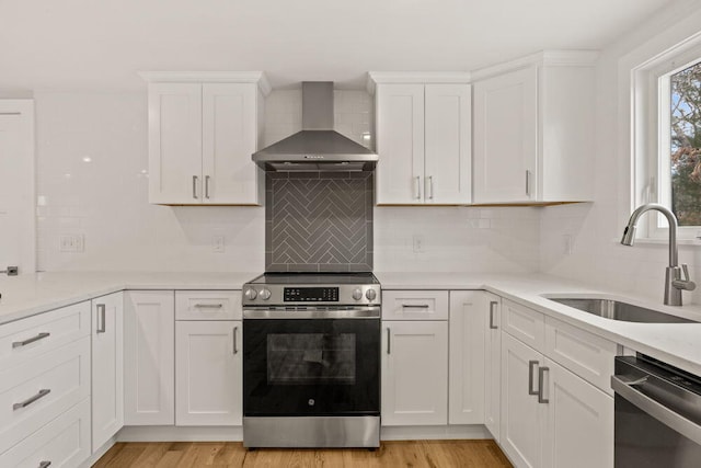 kitchen with a sink, wall chimney exhaust hood, appliances with stainless steel finishes, and white cabinets