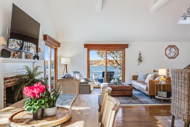 living area with vaulted ceiling with beams, a brick fireplace, a water view, and wood finished floors