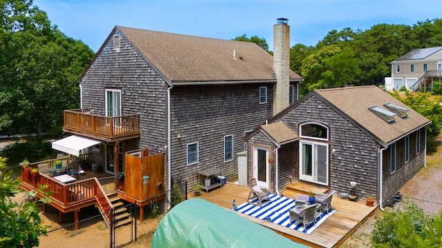 back of property with a chimney, a shingled roof, outdoor dining area, and a deck