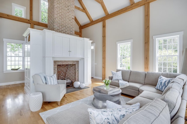 living room featuring high vaulted ceiling, baseboards, beamed ceiling, light wood-style floors, and a fireplace with flush hearth