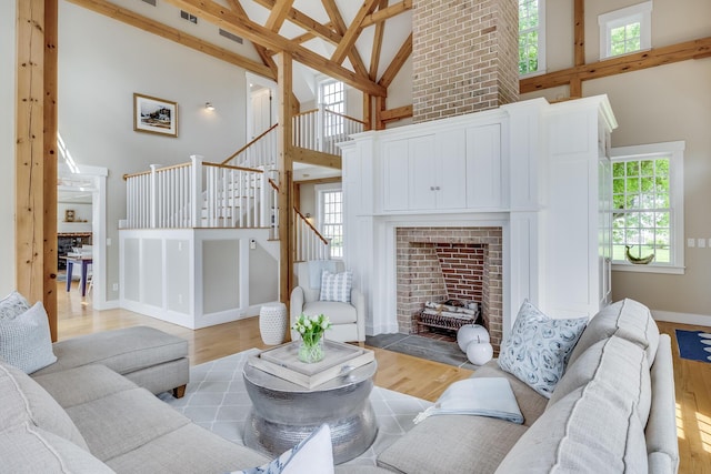 living room featuring high vaulted ceiling, stairway, light wood-style floors, a brick fireplace, and baseboards