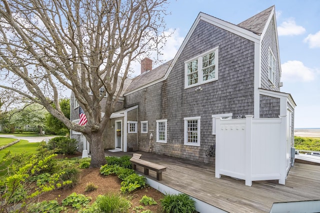 view of property exterior with a wooden deck, a chimney, and a shingled roof