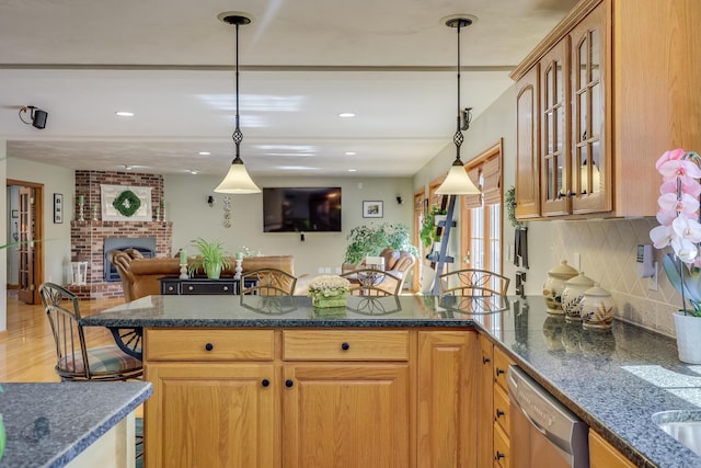 kitchen with pendant lighting, a breakfast bar, dishwasher, tasteful backsplash, and a brick fireplace