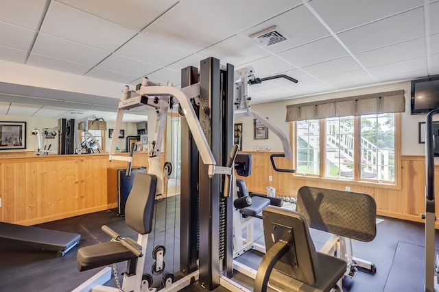 gym featuring a drop ceiling and wood walls