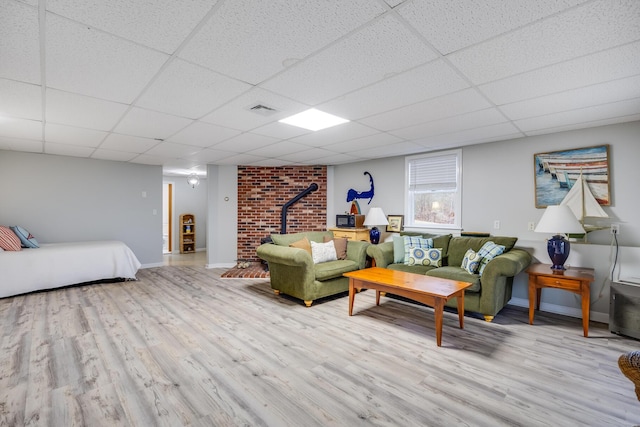 living room featuring a drop ceiling, light hardwood / wood-style flooring, and a wood stove