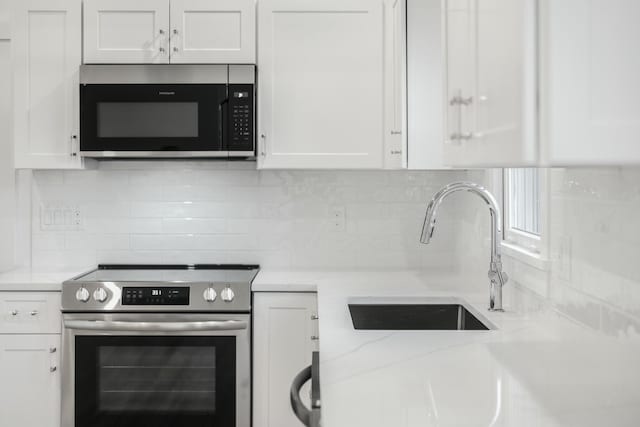 kitchen featuring a sink, backsplash, white cabinetry, and stainless steel appliances