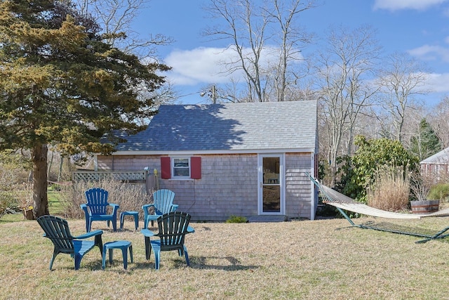back of house with a lawn, a shingled roof, and an outbuilding