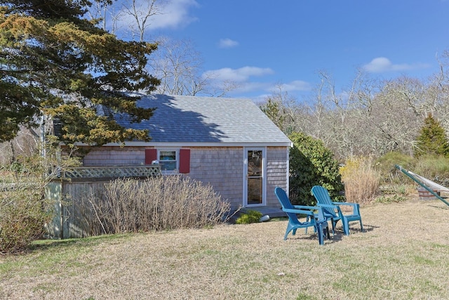rear view of property featuring a shingled roof and a yard