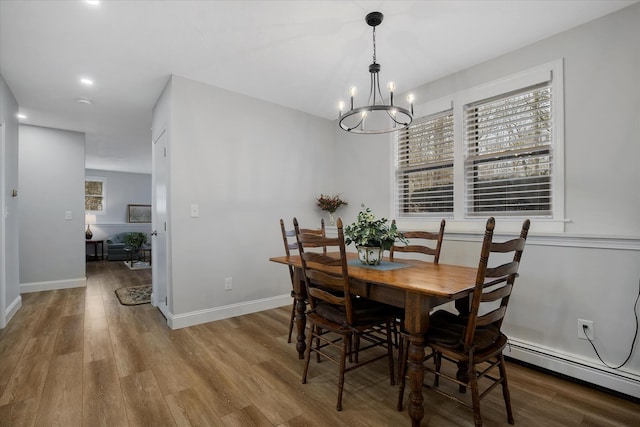 dining area with a chandelier, baseboard heating, wood finished floors, and baseboards