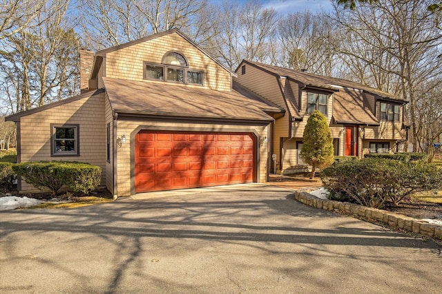 view of front of property featuring driveway, a garage, a chimney, and roof with shingles