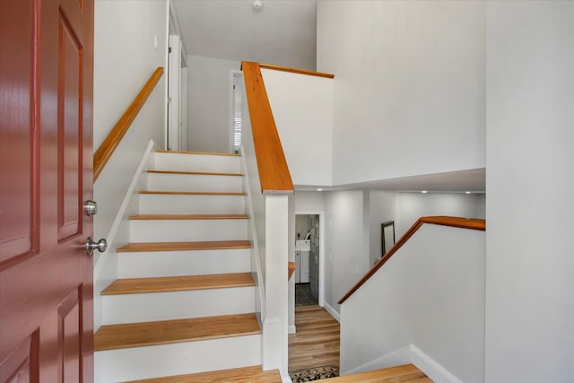 stairway featuring baseboards, a high ceiling, and wood finished floors