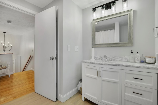 bathroom with a chandelier, vanity, baseboards, and wood finished floors