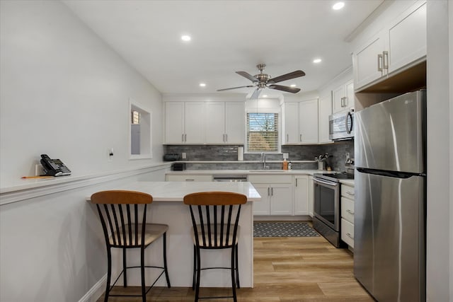 kitchen with a breakfast bar, appliances with stainless steel finishes, white cabinets, a sink, and a peninsula