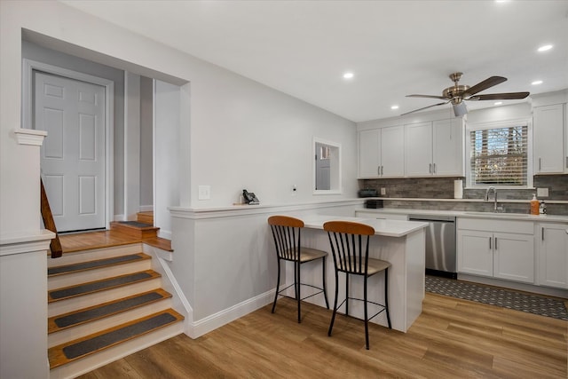 kitchen featuring a kitchen bar, light wood-style floors, dishwasher, and a sink