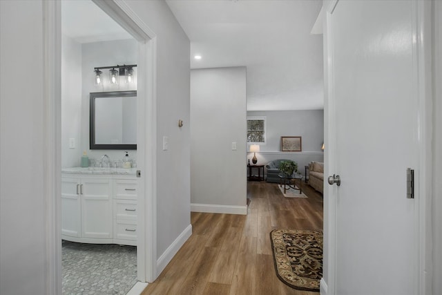 hall featuring light wood-style floors, baseboards, and a sink