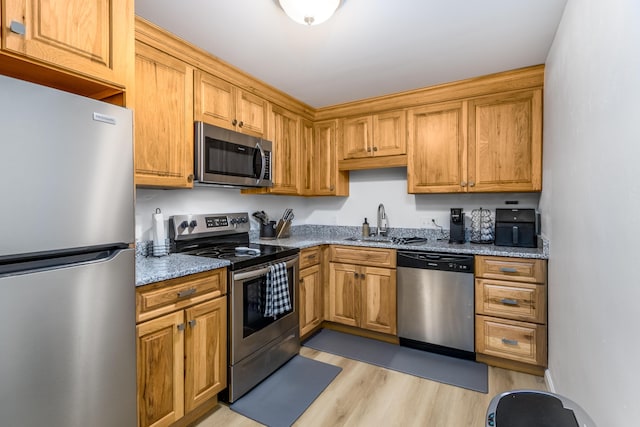 kitchen featuring light stone countertops, light wood-type flooring, appliances with stainless steel finishes, and sink