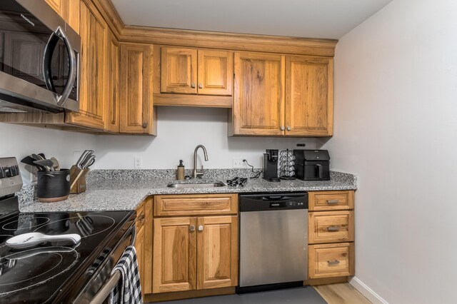 kitchen with sink, stainless steel appliances, light stone counters, and light hardwood / wood-style flooring