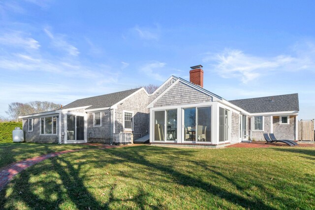 back of property with a sunroom, a chimney, roof with shingles, and a lawn