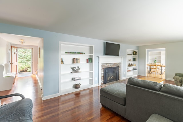 living room with dark wood-type flooring, a fireplace with flush hearth, and built in shelves
