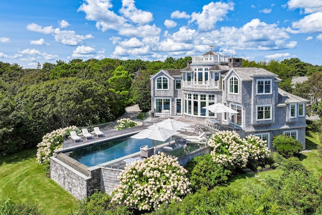 back of property with a patio area, a lawn, a balcony, and an outdoor pool