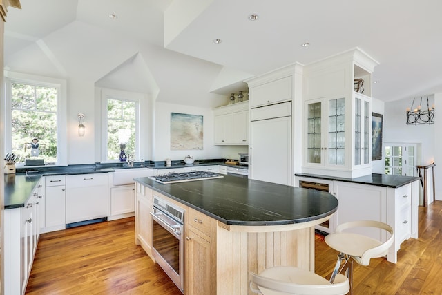 kitchen featuring dark countertops, light wood-style floors, a kitchen island, glass insert cabinets, and appliances with stainless steel finishes