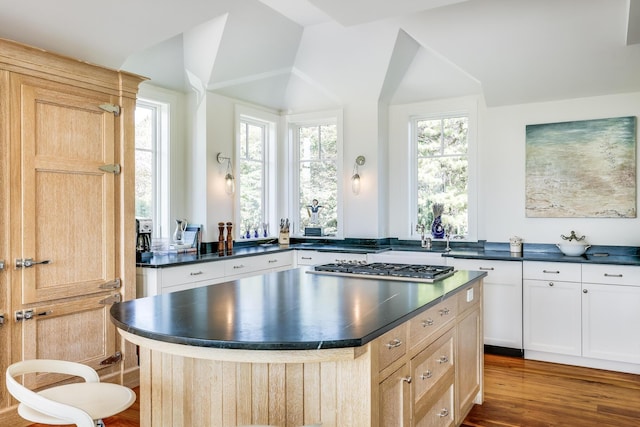 kitchen with a center island, stainless steel gas cooktop, dark countertops, vaulted ceiling, and wood finished floors