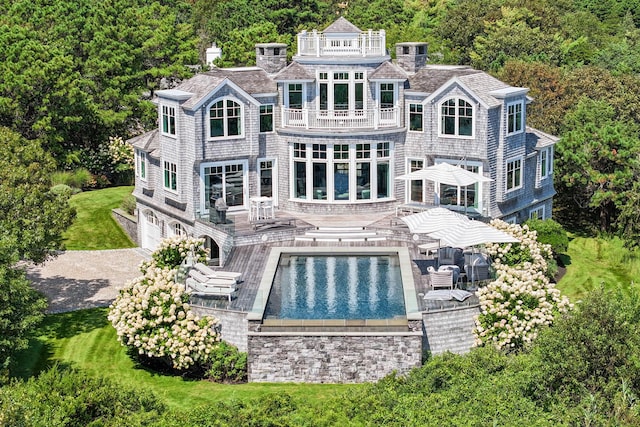 rear view of property featuring a wooded view, an outdoor pool, a balcony, and a garage