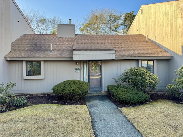 view of front facade featuring a front yard, roof with shingles, and a chimney