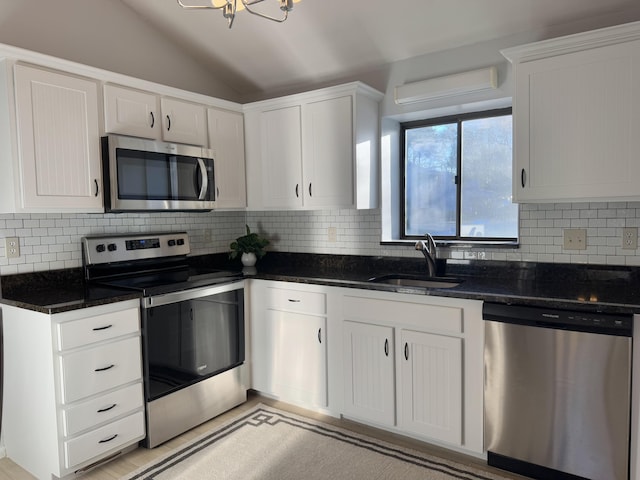 kitchen featuring stainless steel appliances, dark stone counters, white cabinets, and a sink