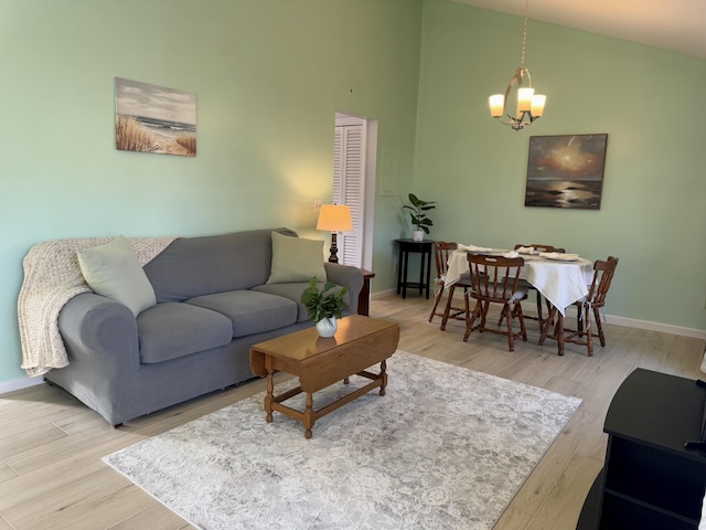 living area with a towering ceiling, a notable chandelier, light wood-style flooring, and baseboards