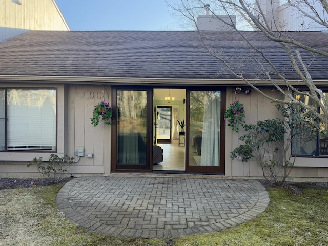 entrance to property featuring a patio and roof with shingles