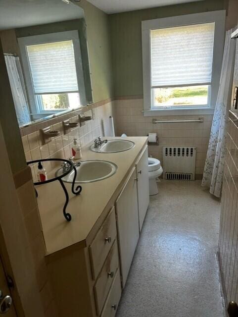 bathroom featuring toilet, radiator, vanity, and tile walls