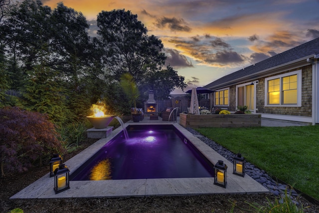 pool at dusk featuring a yard, a patio, an outdoor fire pit, fence, and an outdoor pool