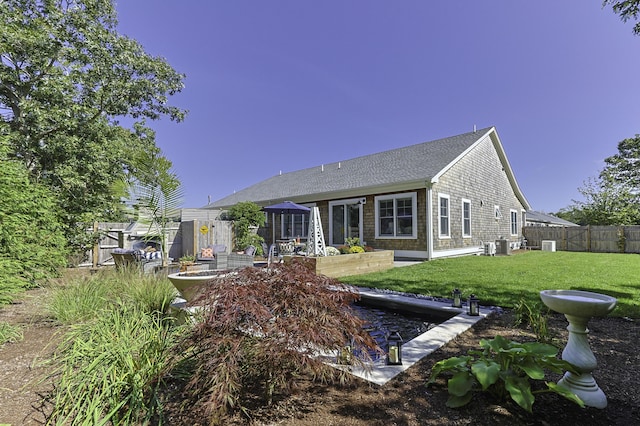 rear view of house featuring a yard, a shingled roof, and fence