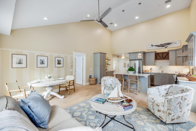 living area featuring ceiling fan, high vaulted ceiling, visible vents, and light wood-style floors