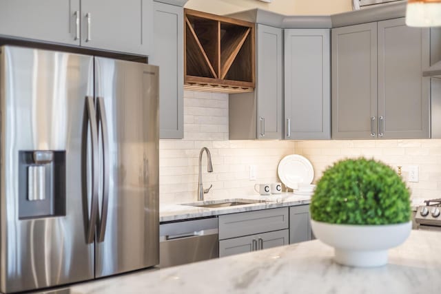 kitchen featuring appliances with stainless steel finishes, gray cabinets, a sink, and light stone countertops