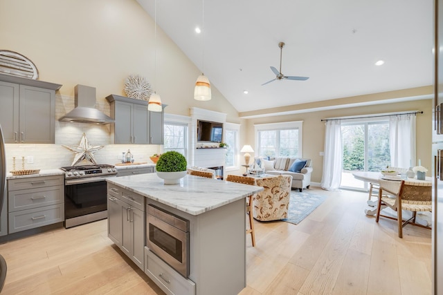 kitchen with a center island, gray cabinetry, appliances with stainless steel finishes, open floor plan, and wall chimney exhaust hood