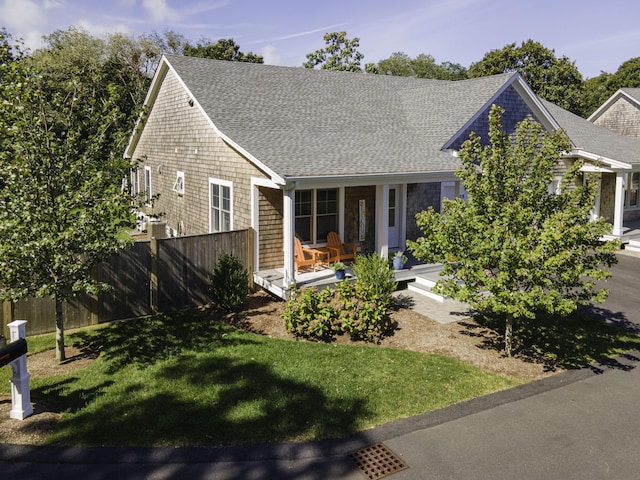 view of front of house featuring covered porch, roof with shingles, fence, and a front yard