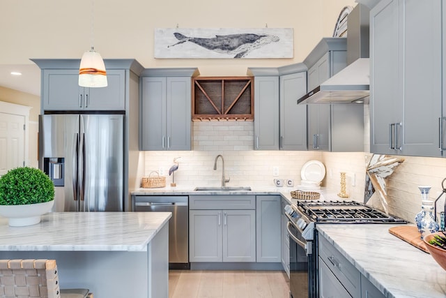 kitchen with a sink, appliances with stainless steel finishes, wall chimney range hood, and light stone counters