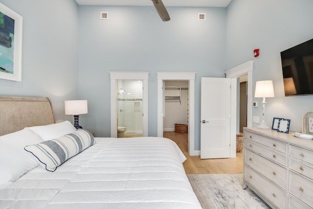 bedroom featuring visible vents, a towering ceiling, ensuite bath, light wood-style flooring, and a walk in closet