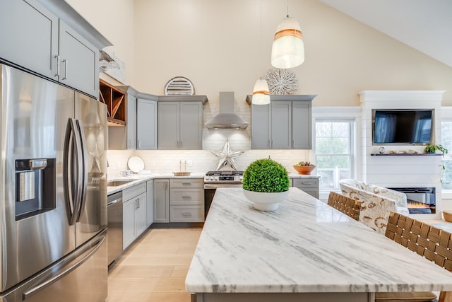 kitchen with high vaulted ceiling, gray cabinetry, stainless steel appliances, a kitchen island, and wall chimney exhaust hood