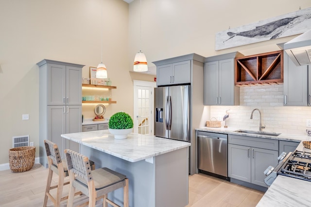 kitchen with stainless steel appliances, gray cabinets, a sink, and light stone countertops