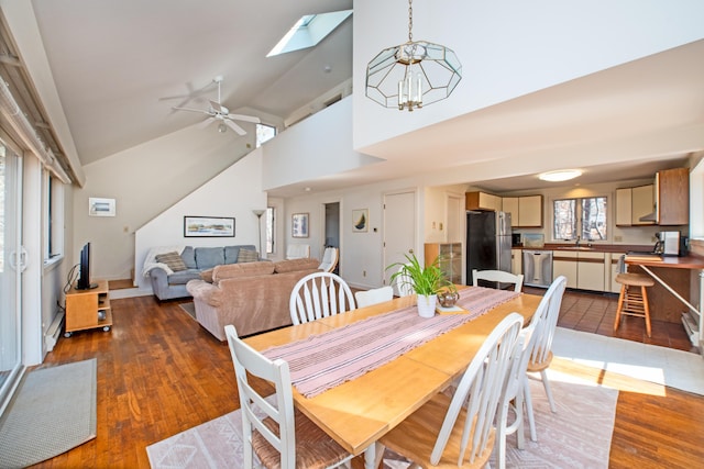 dining room with ceiling fan with notable chandelier, high vaulted ceiling, dark wood-type flooring, and a skylight