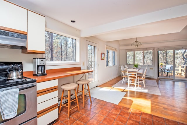 kitchen featuring under cabinet range hood, electric range, a breakfast bar, white cabinetry, and light countertops