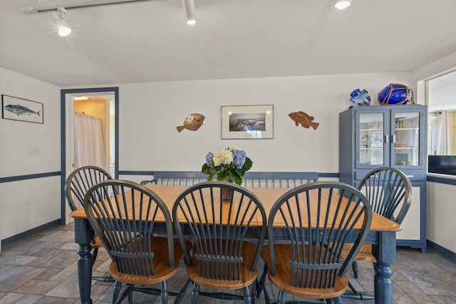 dining room featuring rail lighting, stone tile flooring, and baseboards