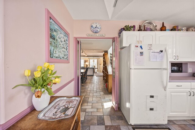 kitchen featuring white cabinets, stone finish floor, and freestanding refrigerator