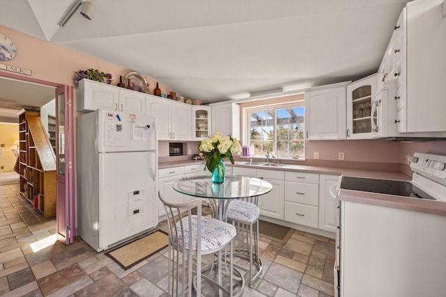 kitchen with a sink, stone tile flooring, glass insert cabinets, white appliances, and white cabinets