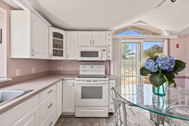 kitchen featuring glass insert cabinets, white appliances, white cabinetry, light countertops, and lofted ceiling